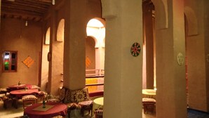 Un intérieur traditionnel doté de plusieurs espaces de détente, comprenant des tables rondes et des bancs, sous un haut plafond en bois orné d’arches.