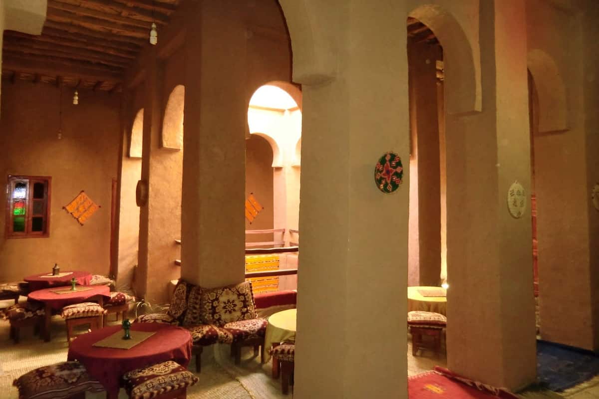 Un intérieur traditionnel doté de plusieurs espaces de détente, comprenant des tables rondes et des bancs, sous un haut plafond en bois orné d’arches.