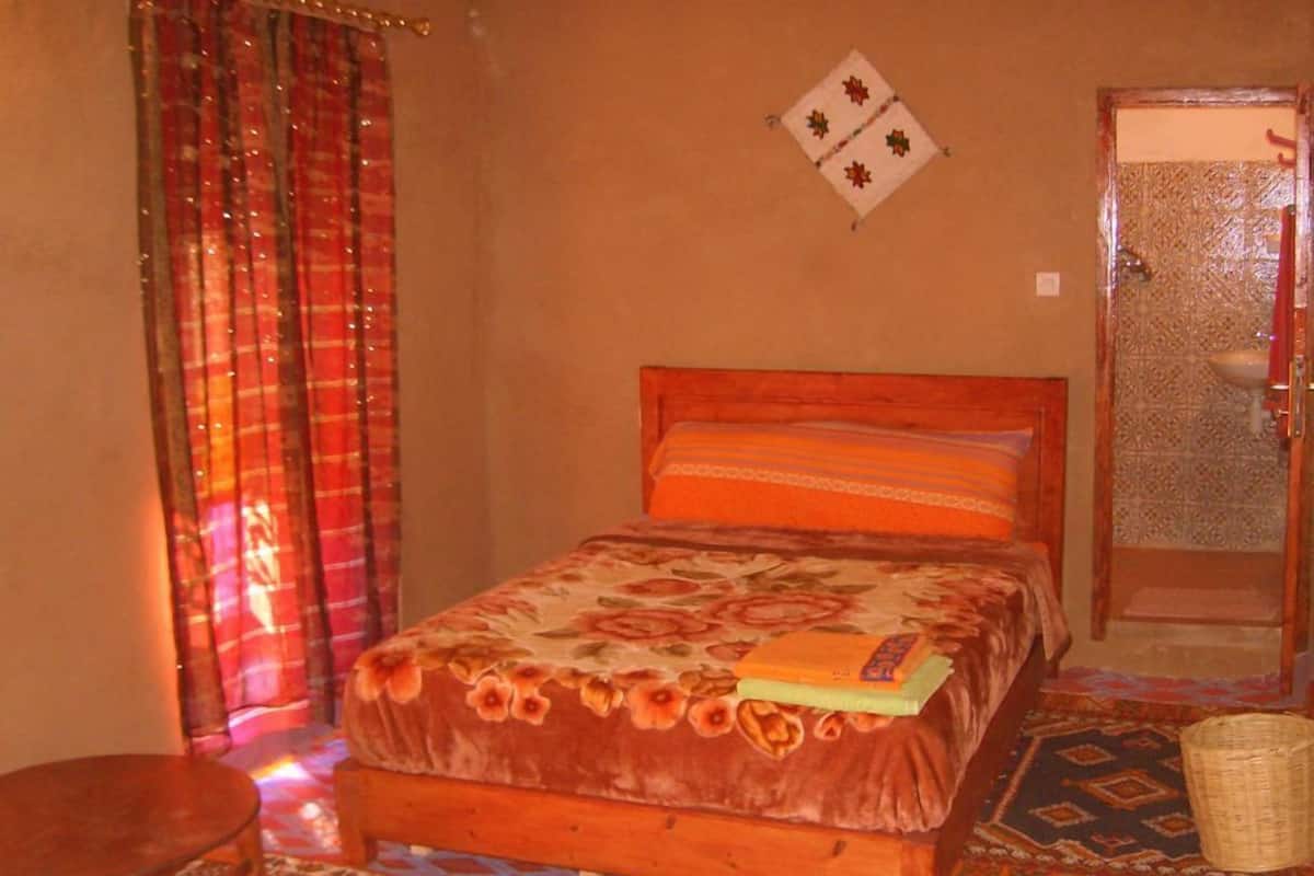 Une chambre à coucher avec un lit en bois, un tapis à motifs, une petite table et une décoration murale.