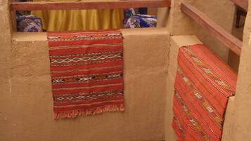 A narrow, enclosed space with a wooden railing, a yellow table, and a red patterned cloth hanging on the wall.