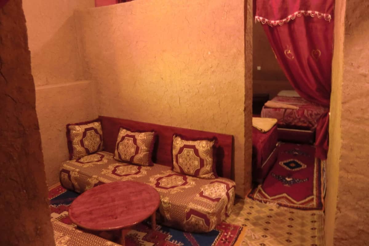 Une pièce chaleureuse avec un canapé et une petite table ronde, un tapis à motifs et un lit surmonté d’un baldaquin rouge.