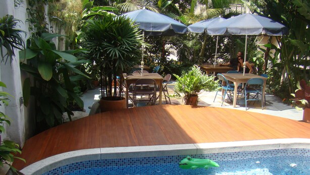 A swimming pool with a wooden deck, surrounded by potted plants and outdoor furniture. - Jardin Azul - Casa Hotel (Cali)
