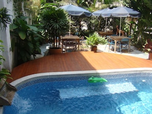 A swimming pool with a wooden deck, surrounded by potted plants and outdoor furniture. - Jardin Azul - Casa Hotel (Cali)