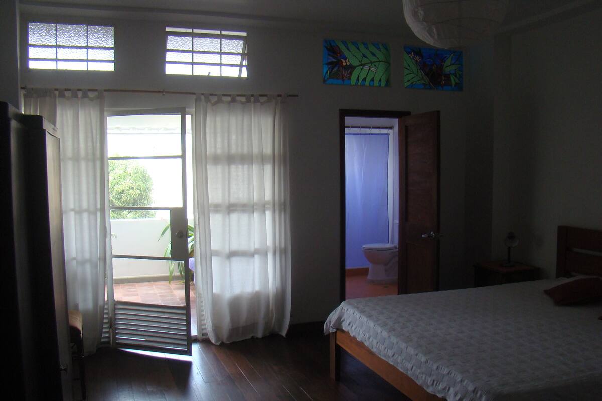 A bedroom with a bed, a door leading to a bathroom, and a view through a window.