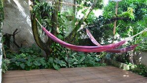 A hammock suspended between trees in a lush garden with a wooden deck. - Jardin Azul - Casa Hotel (Cali)