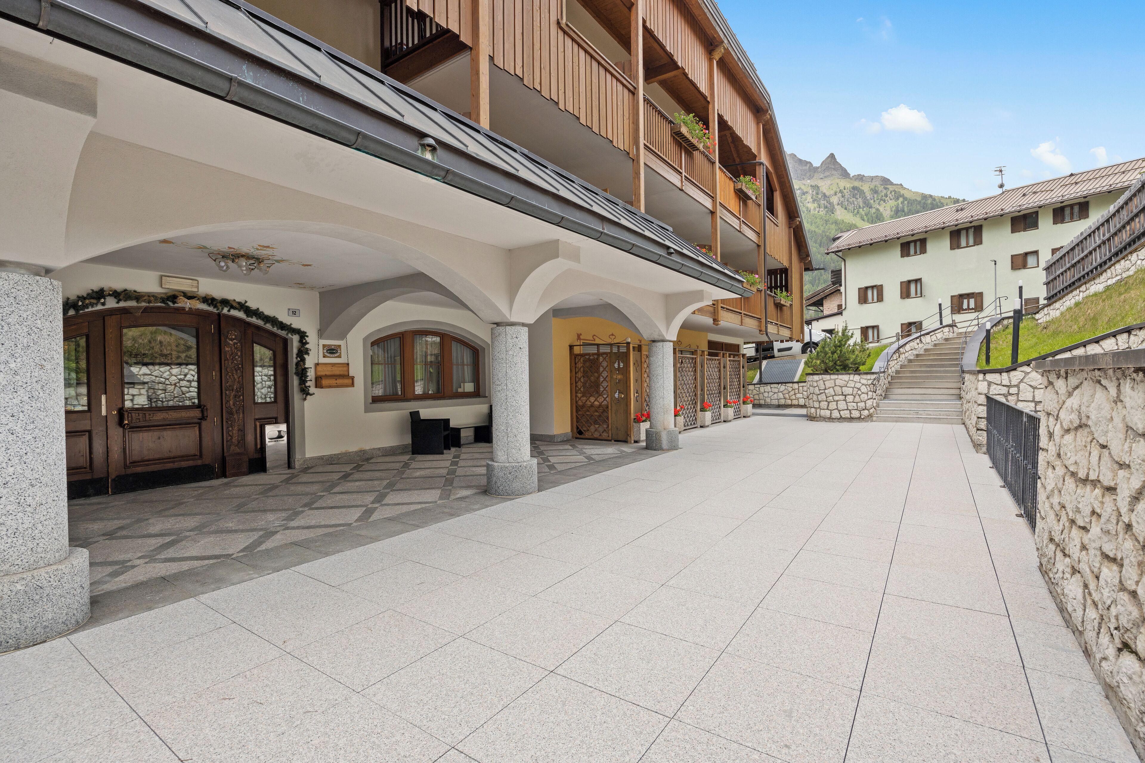 Un hôtel doté d’un espace extérieur abrité, agrémenté de colonnes en pierre, de balcons en bois et d’un escalier en pierre menant à un point de vue sur la montagne.