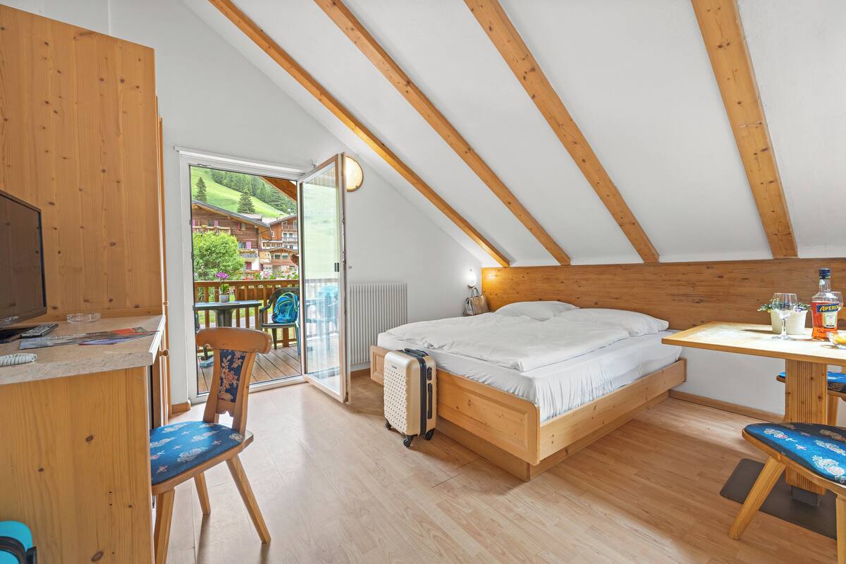 A bedroom with a wooden ceiling, a bed, a desk, and a chair.