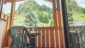 Une terrasse en bois avec une table et des chaises, offrant une vue sur un paysage montagneux, avec des arbres et un ciel dégagé.