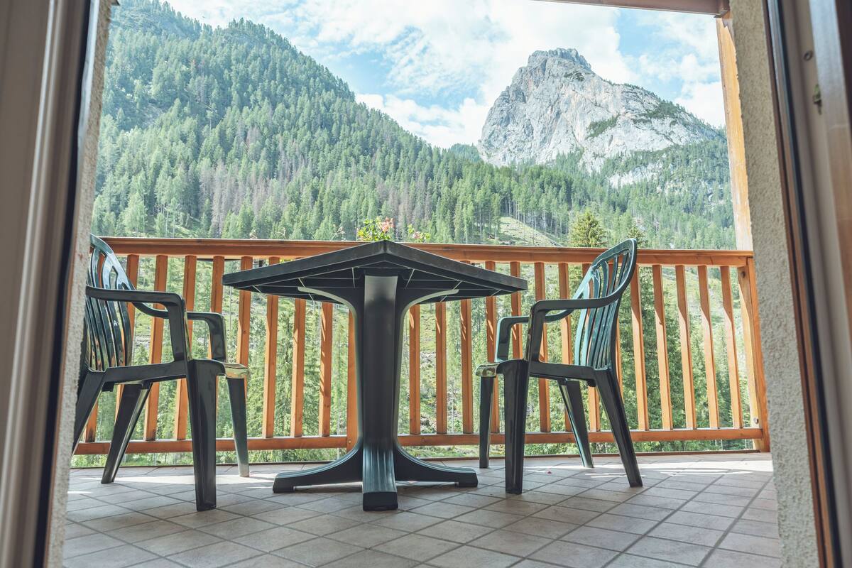 A balcony with a table and chairs, offering a view of a forested mountain range.