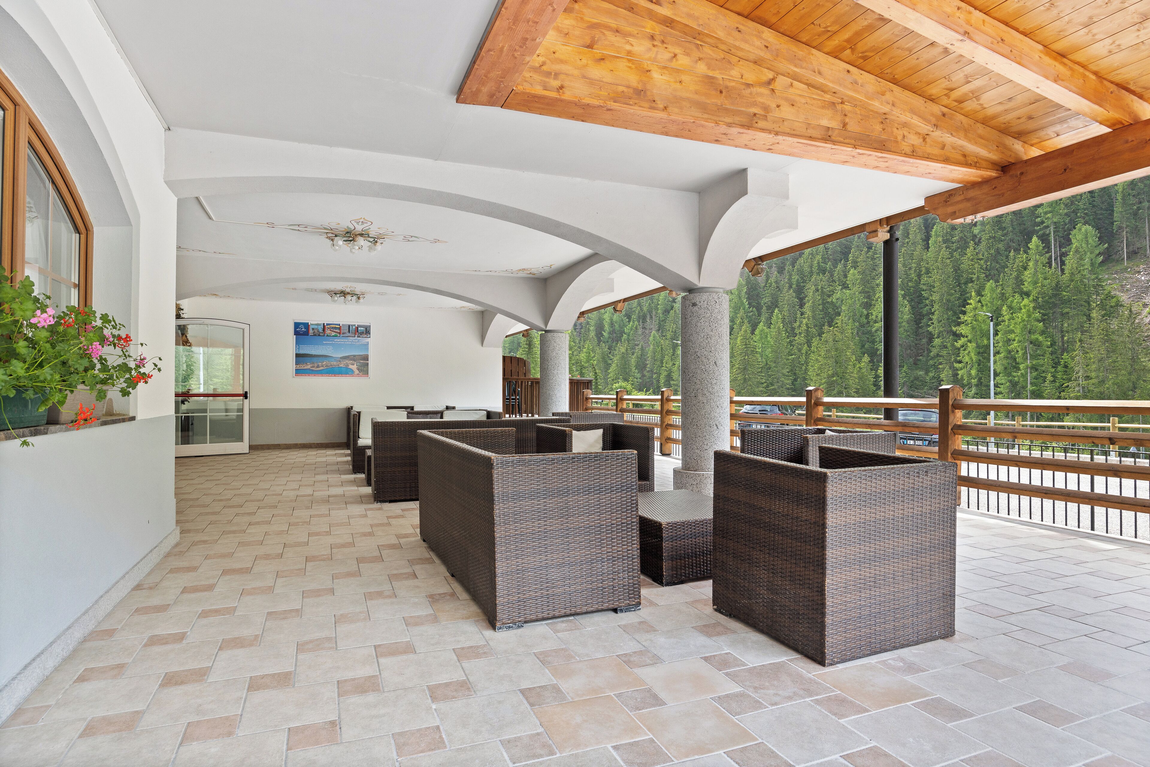 A covered outdoor seating area with wicker furniture, a tiled floor, and a view of a forested mountain.