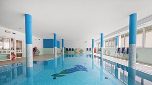 Une piscine intérieure aux murs recouverts de mosaïques bleues, à l’eau claire, et ornée de piliers bleus.
