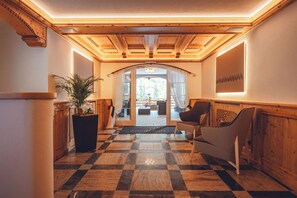 A hotel lobby with a checkered floor, wooden paneling, a potted plant, and a view through a glass door to an outdoor seating area. - Aparthotel Princess (Canazei)