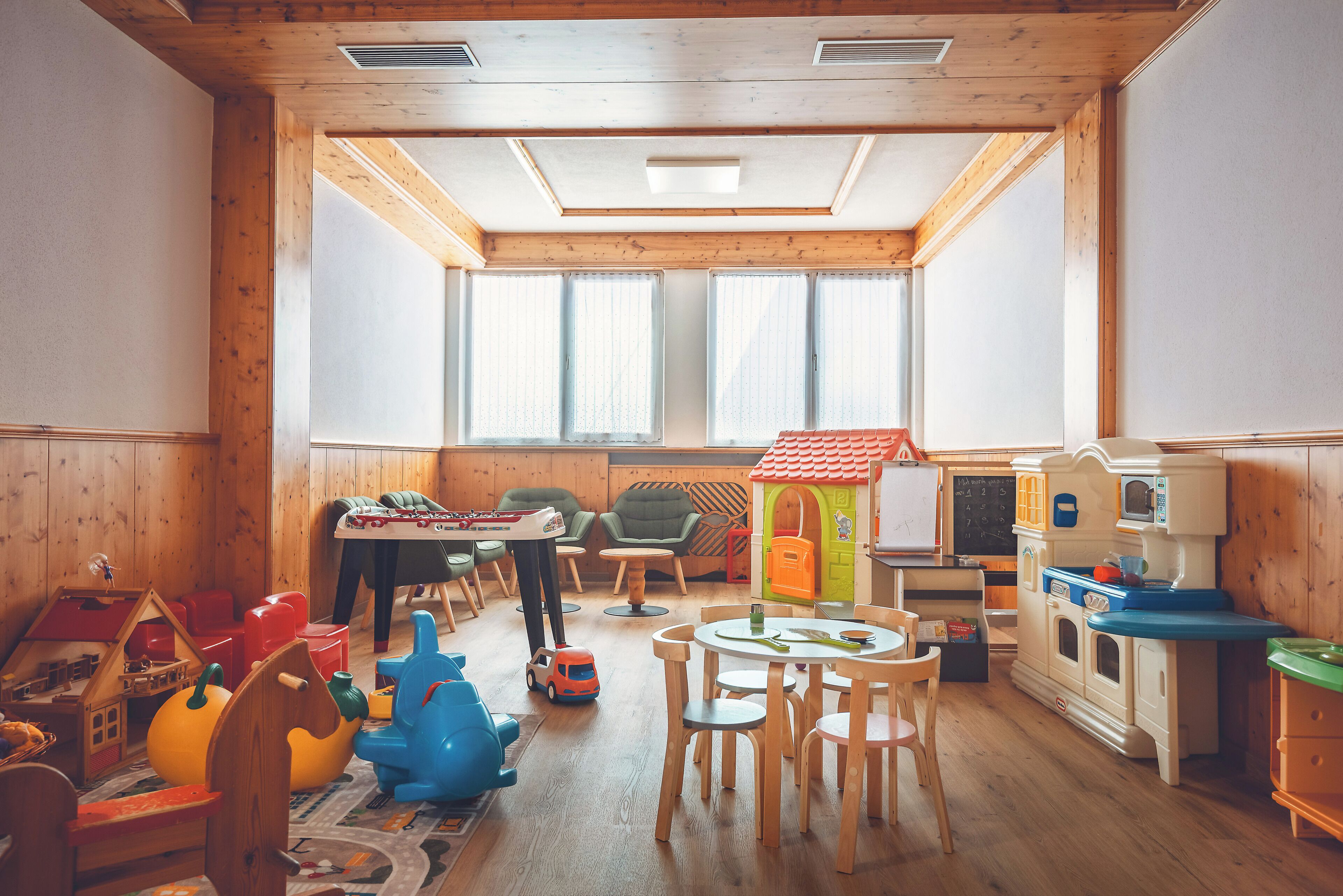 Een kinderspeelruimte met houten wanden, een hoge plafond en grote ramen.