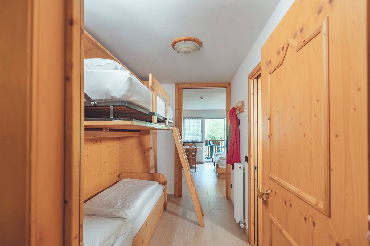 A wooden bunk bed room with a ladder, a wooden door, and a view to a balcony.