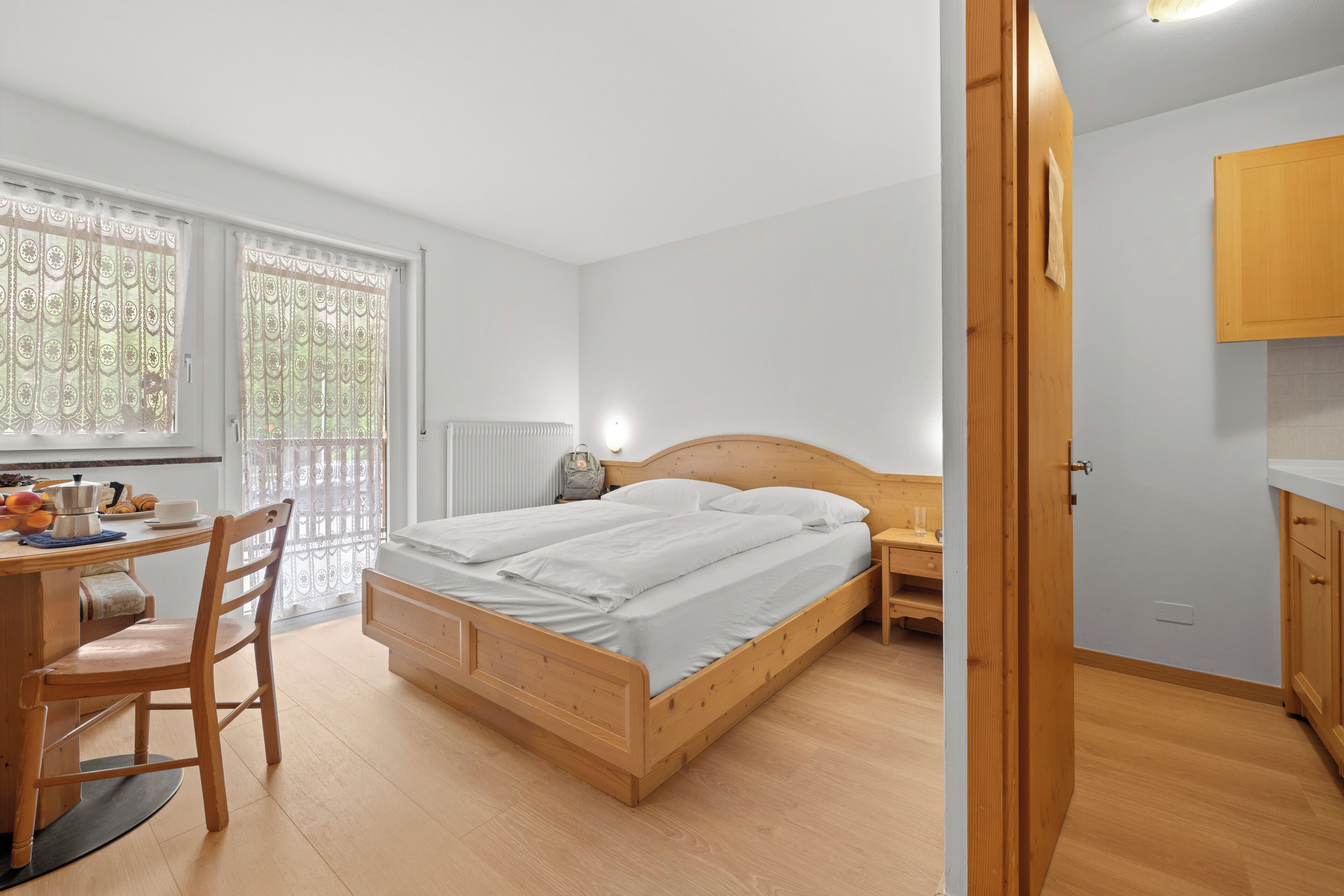 A bedroom with a wooden bed, a desk with a chair, a radiator, and a window with curtains.