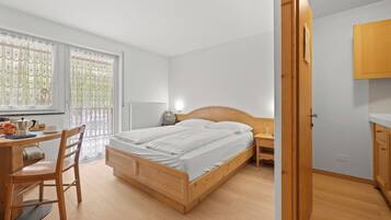 A bedroom with a wooden bed, a desk with a chair, a radiator, and a window with curtains.