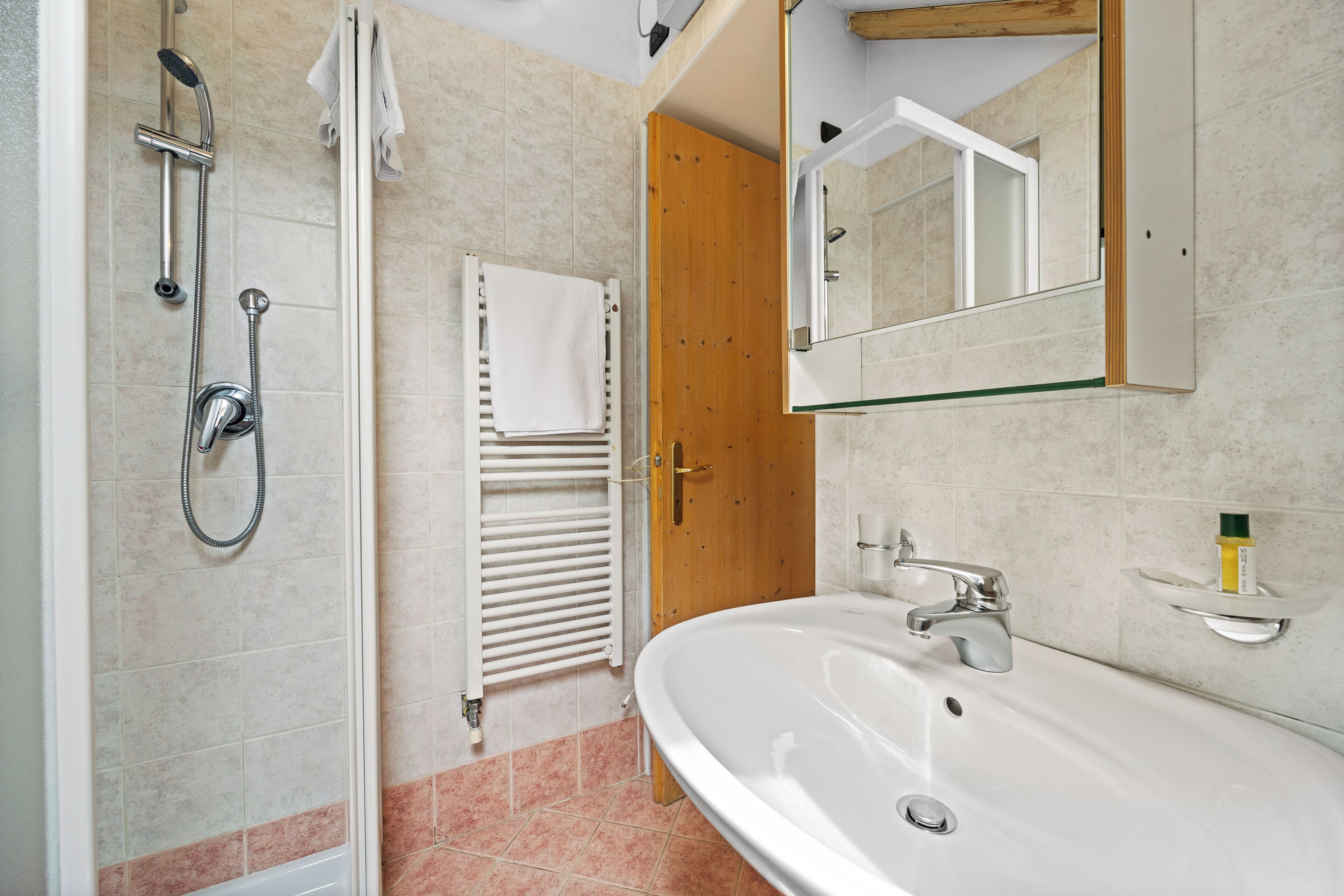 A bathroom with a shower, a sink, a mirror, and a towel rack.