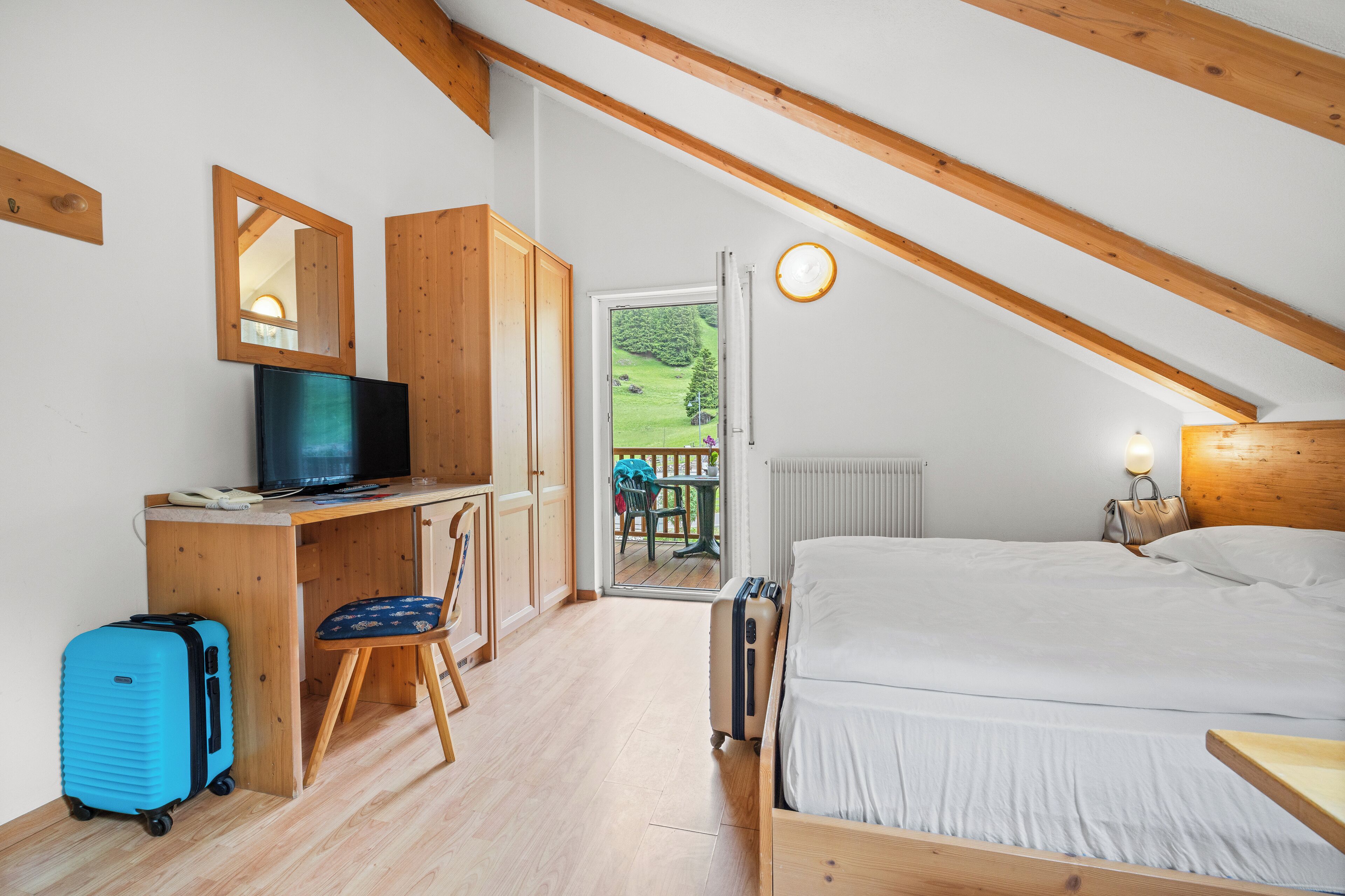 A bedroom with a bed, a desk with a television, a chair, and a suitcase.