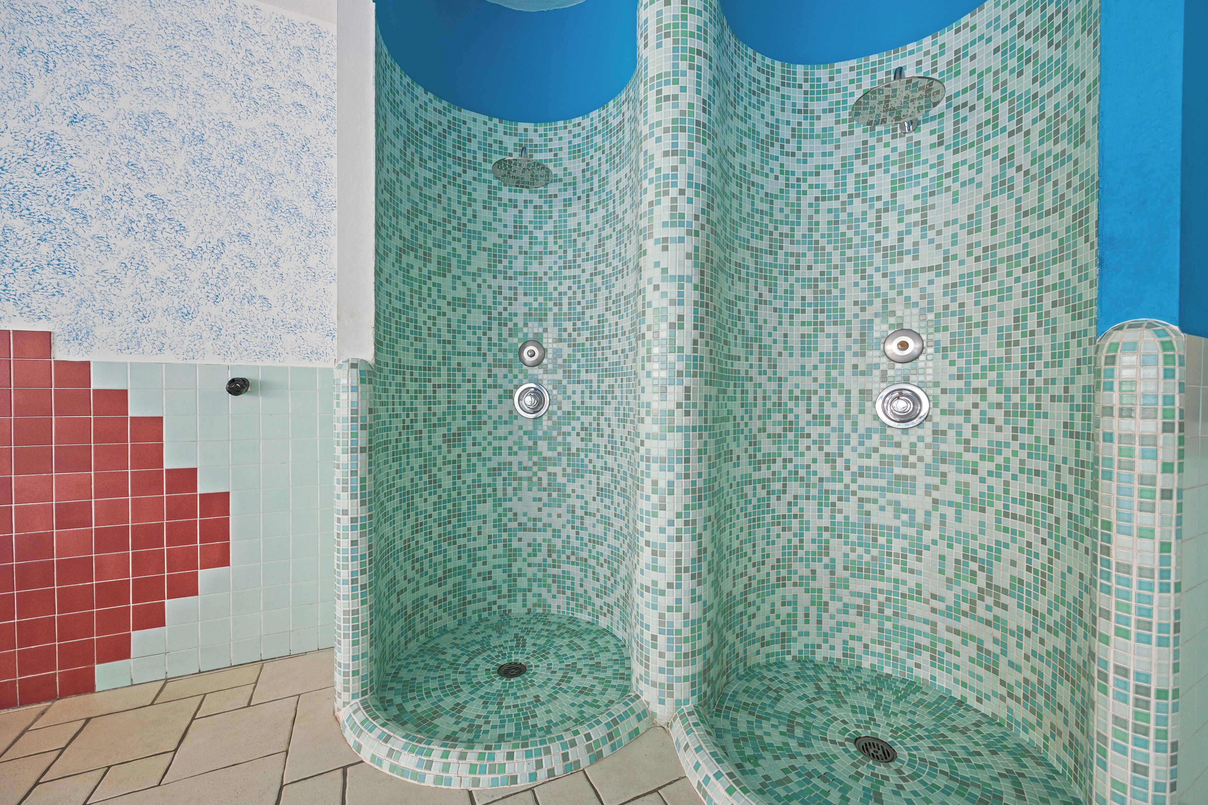 Une salle de bain aux murs recouverts de mosaïques et au sol carrelé de dalles rouges.