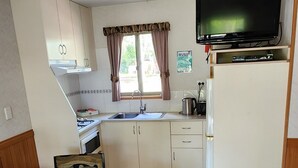 A compact kitchen with a dining table, chairs, a TV, and a refrigerator. - Nitmiluk Cabins (Nitmiluk)