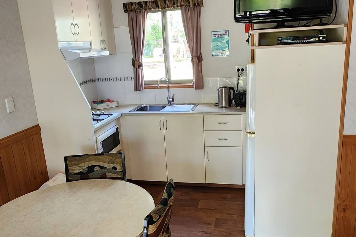 Una cocina compacta con una mesa de comedor, sillas, televisor y refrigerador.