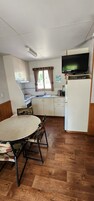 Una cocina compacta con una mesa de comedor, sillas, televisor y refrigerador.