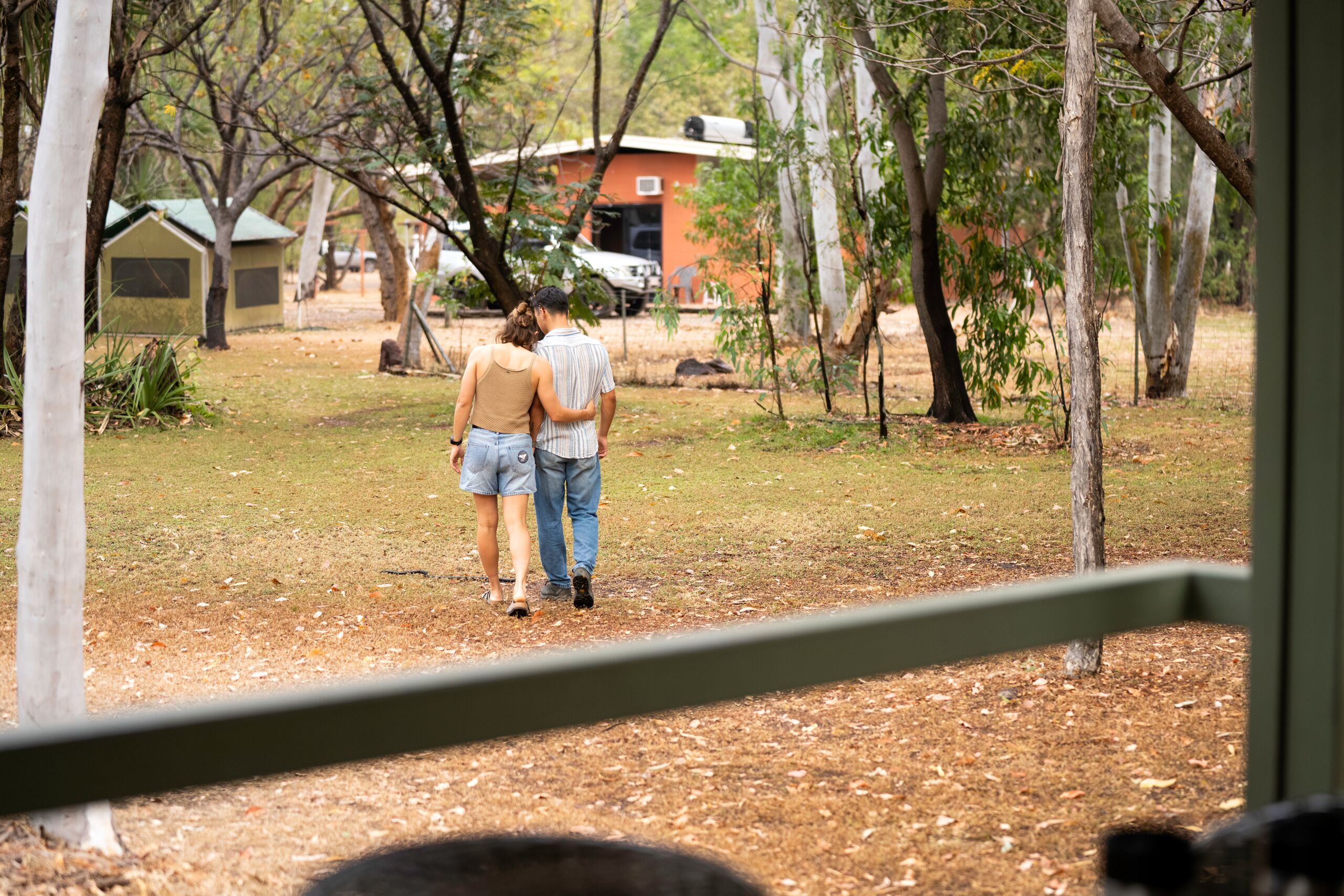 Una pareja caminando en un parque con árboles y un edificio al fondo.
