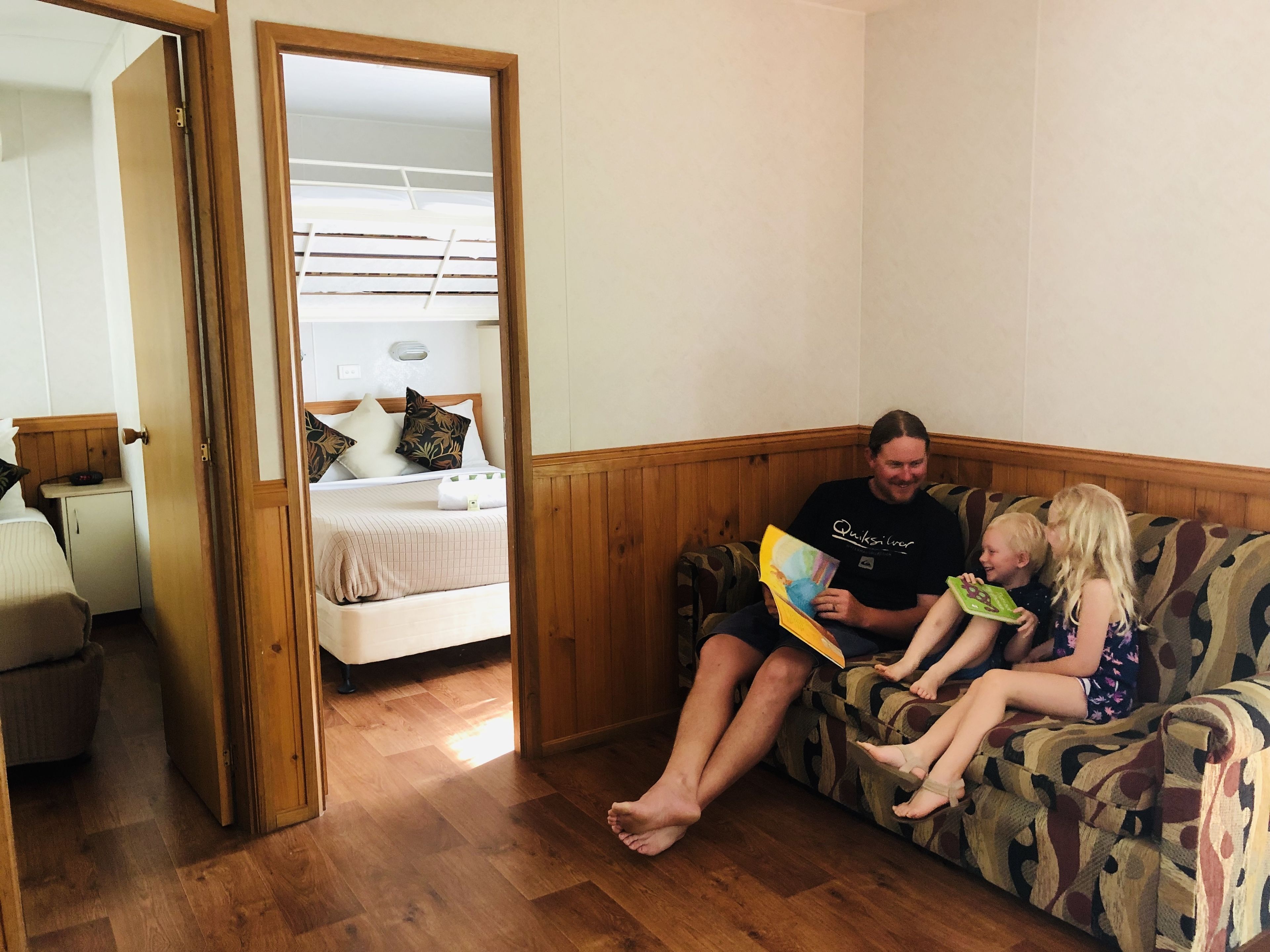 A room with a bed, a wooden floor, a couch, and a door leading to another room.