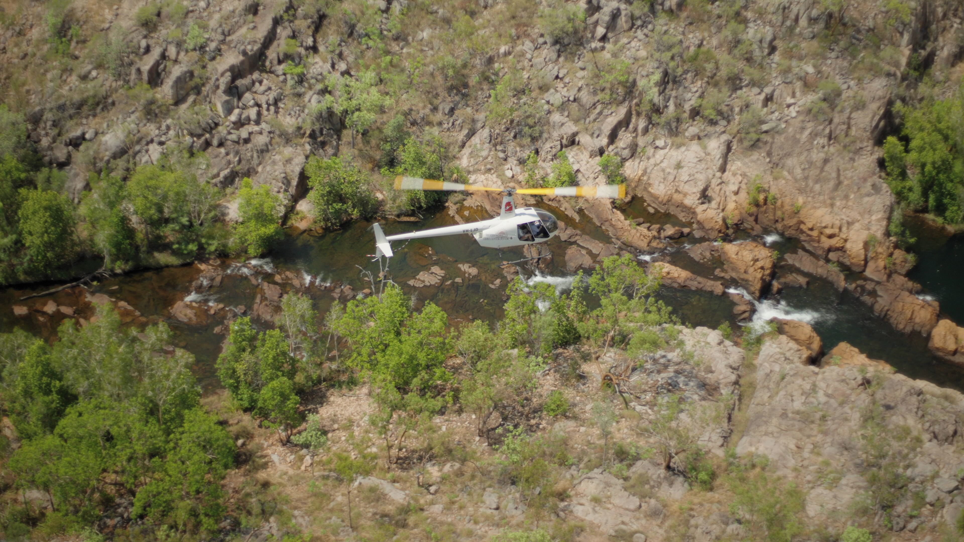 A helicopter flying over a rocky terrain with a river below.
