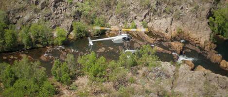 A helicopter flying over a rocky terrain with a river below.