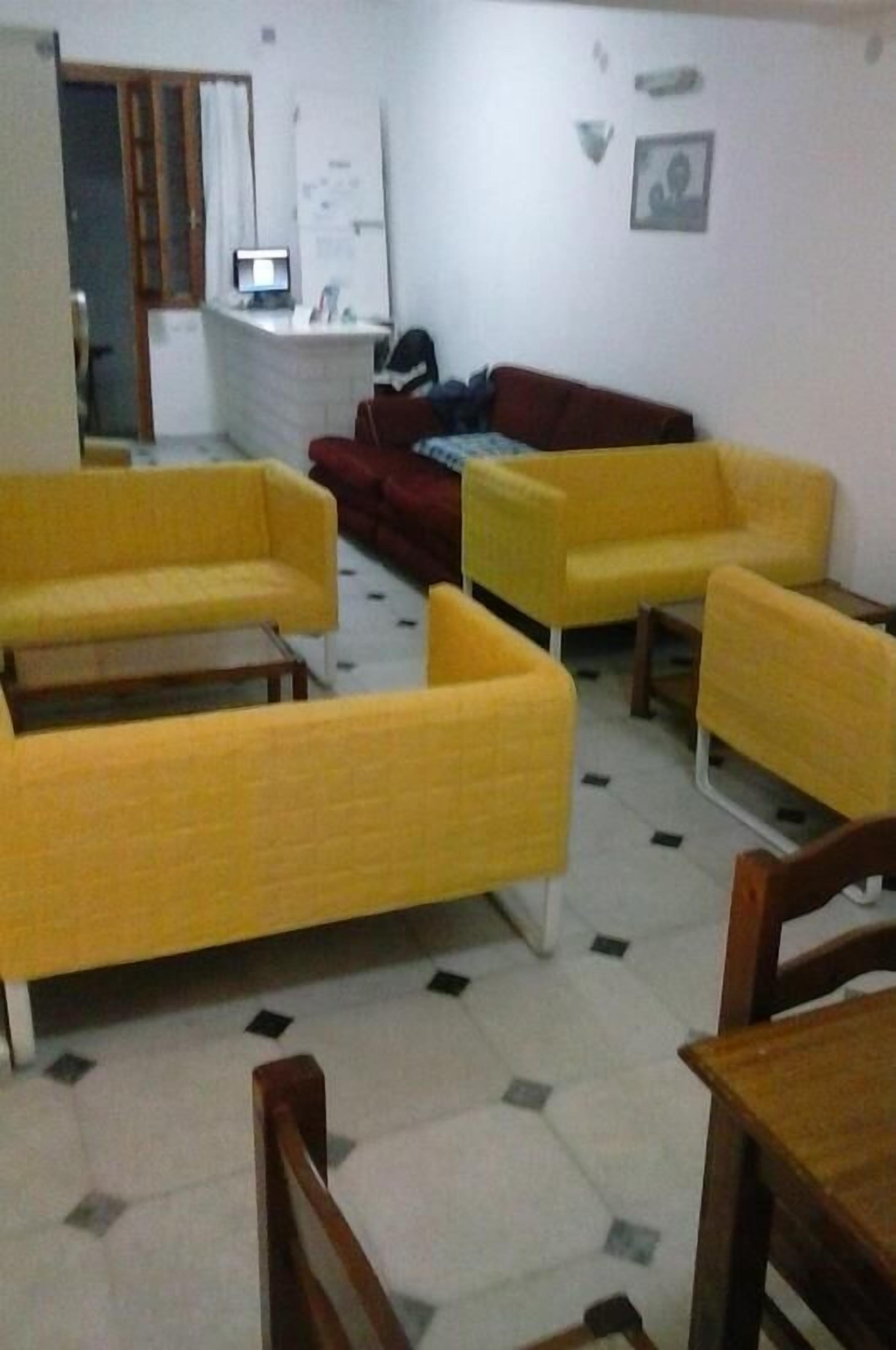 A room with yellow sofas, a red couch, a small table, and a computer on a desk.