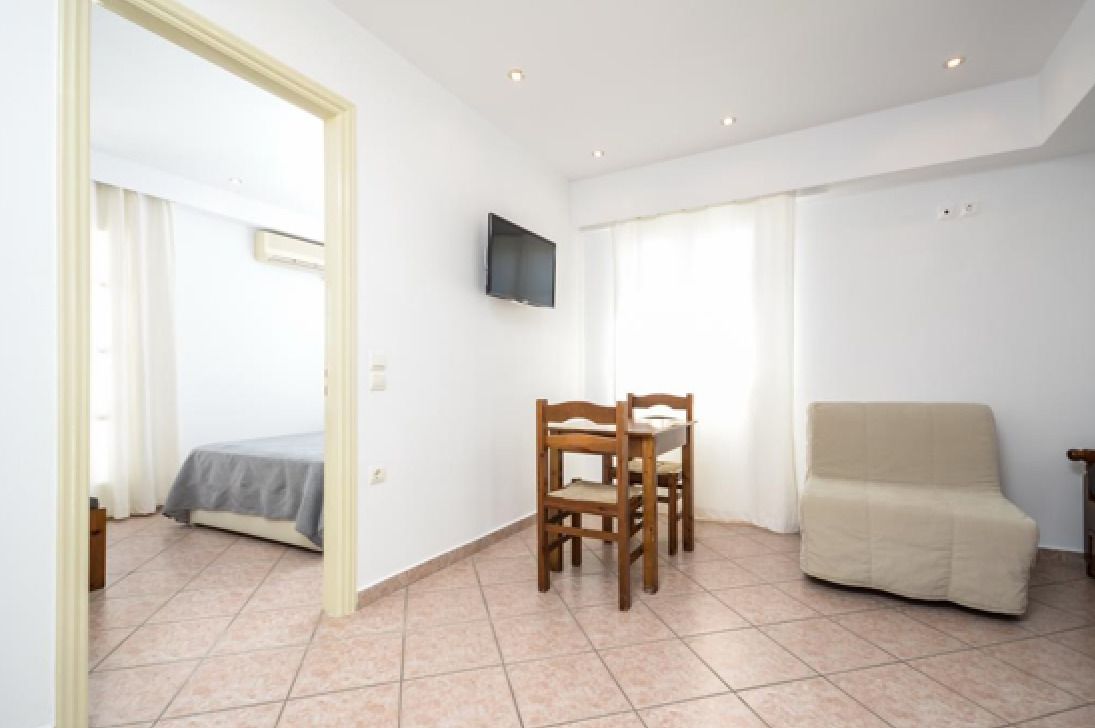 A room with a bed, a TV mounted on the wall, a dining table with chairs, and a sofa.