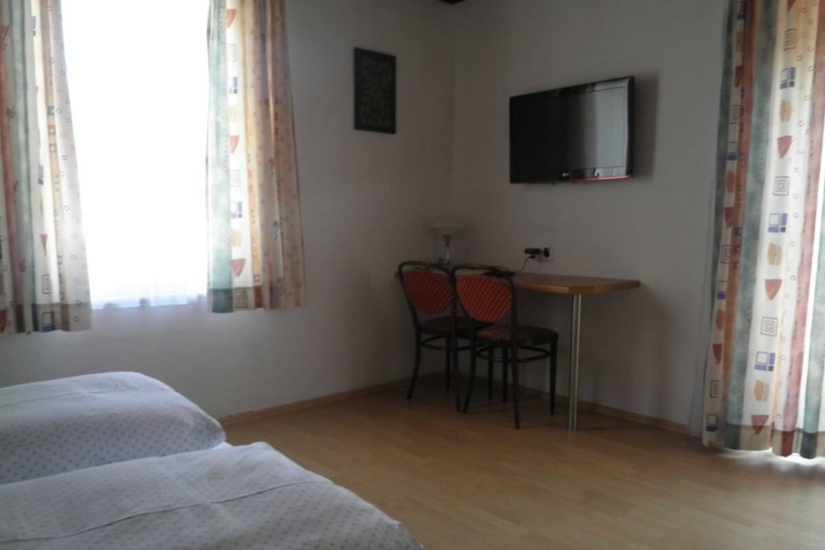 Ein Zimmer mit zwei Betten, einem Schreibtisch, einem Stuhl, einem Fernseher und Vorhängen.