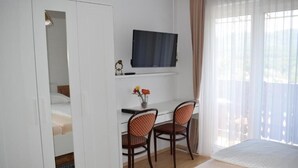 Une chambre d’hôtel comprenant un lit, un bureau avec deux chaises, une télévision et une fenêtre avec des rideaux.