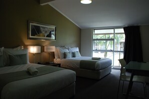 Une chambre d’hôtel avec deux lits, un bureau et une fenêtre donnant sur des palmiers.