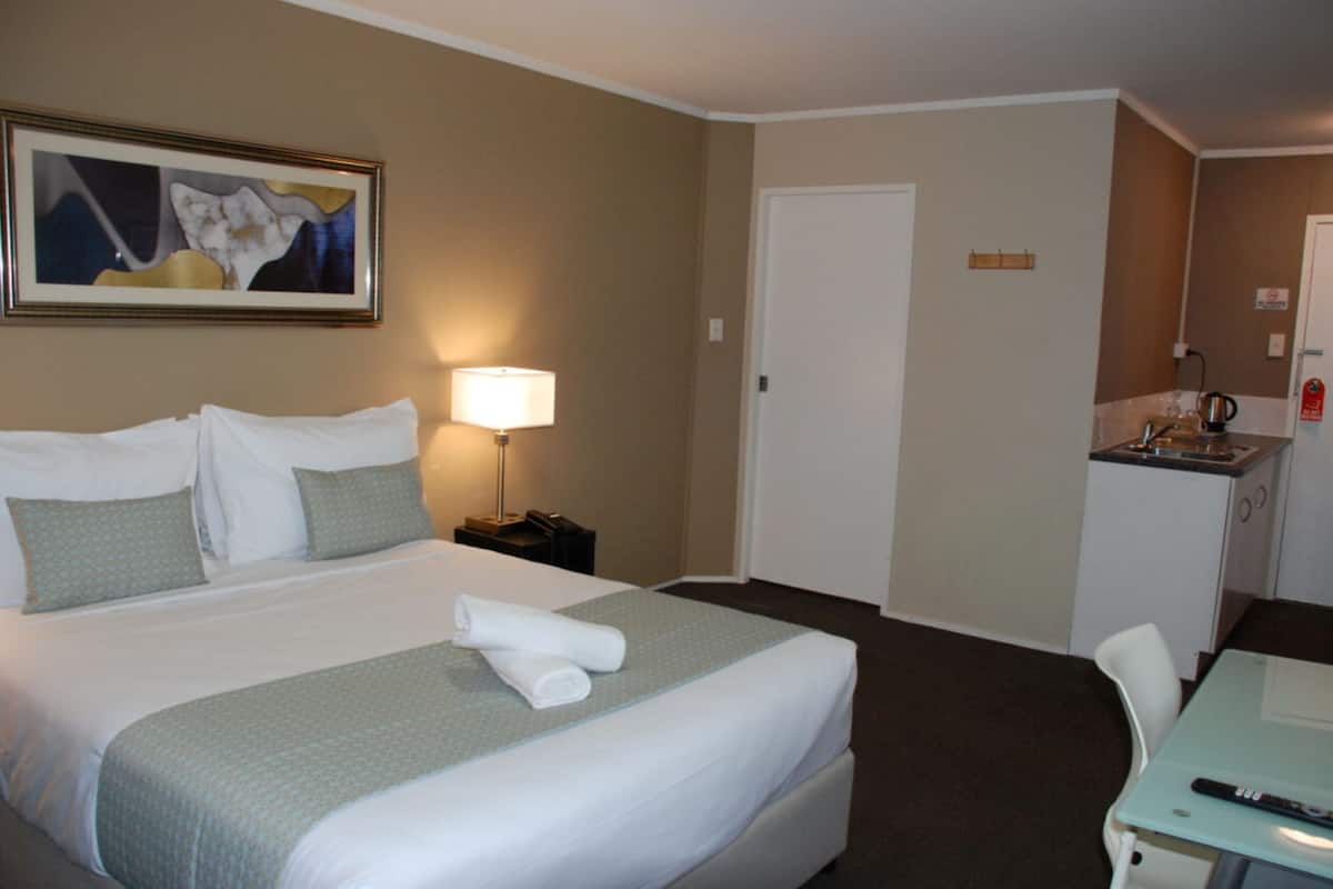 A hotel room with a large bed, a desk, a chair, a lamp, and a painting on the wall.