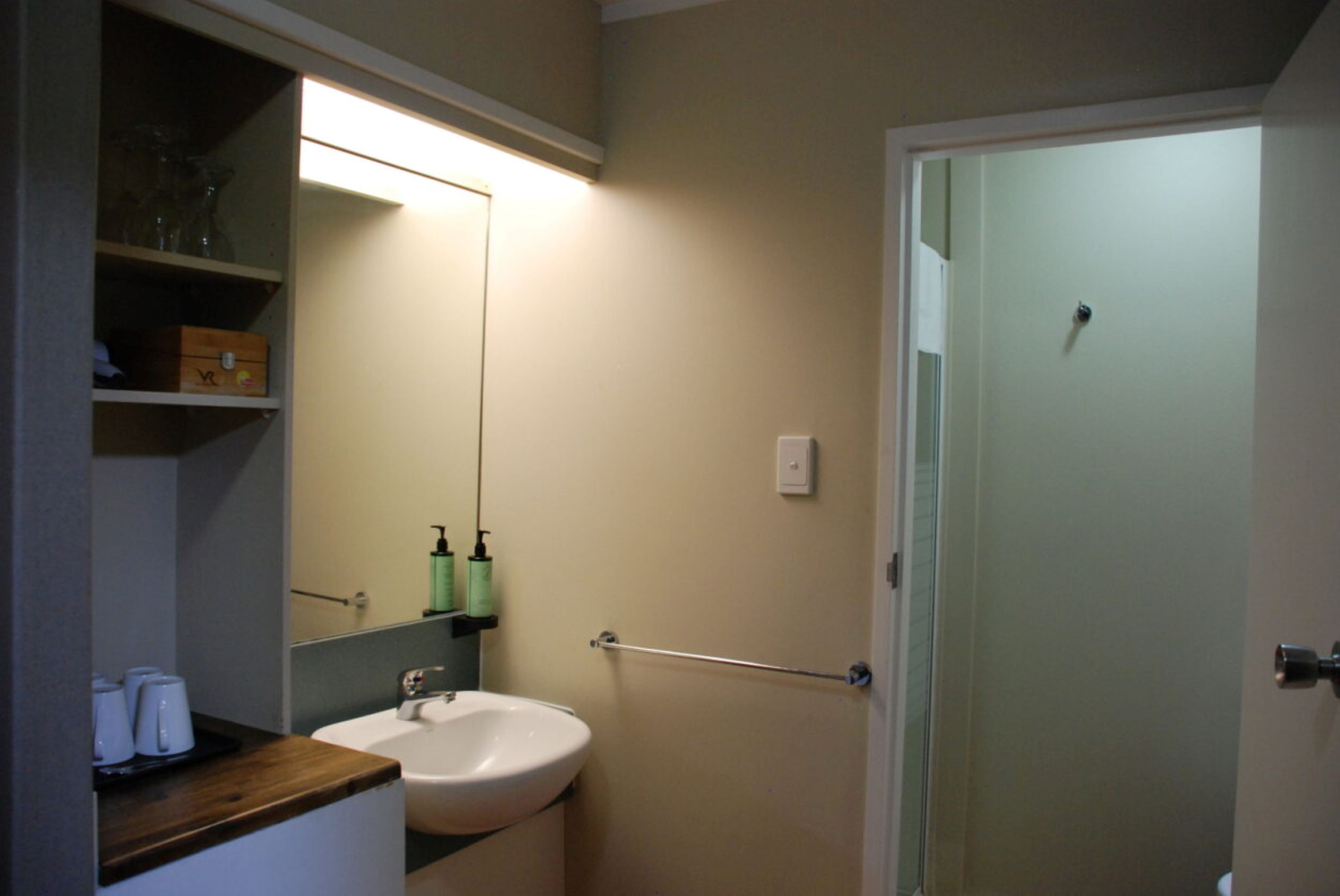 Un baño con lavamanos, espejo y repisas con artículos de aseo.