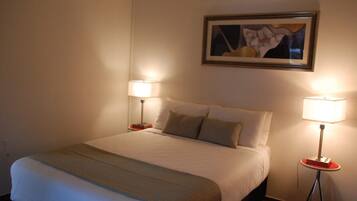 Una habitación de hotel con una cama grande, dos mesitas de noche con lámparas, y un cuadro enmarcado en la pared.