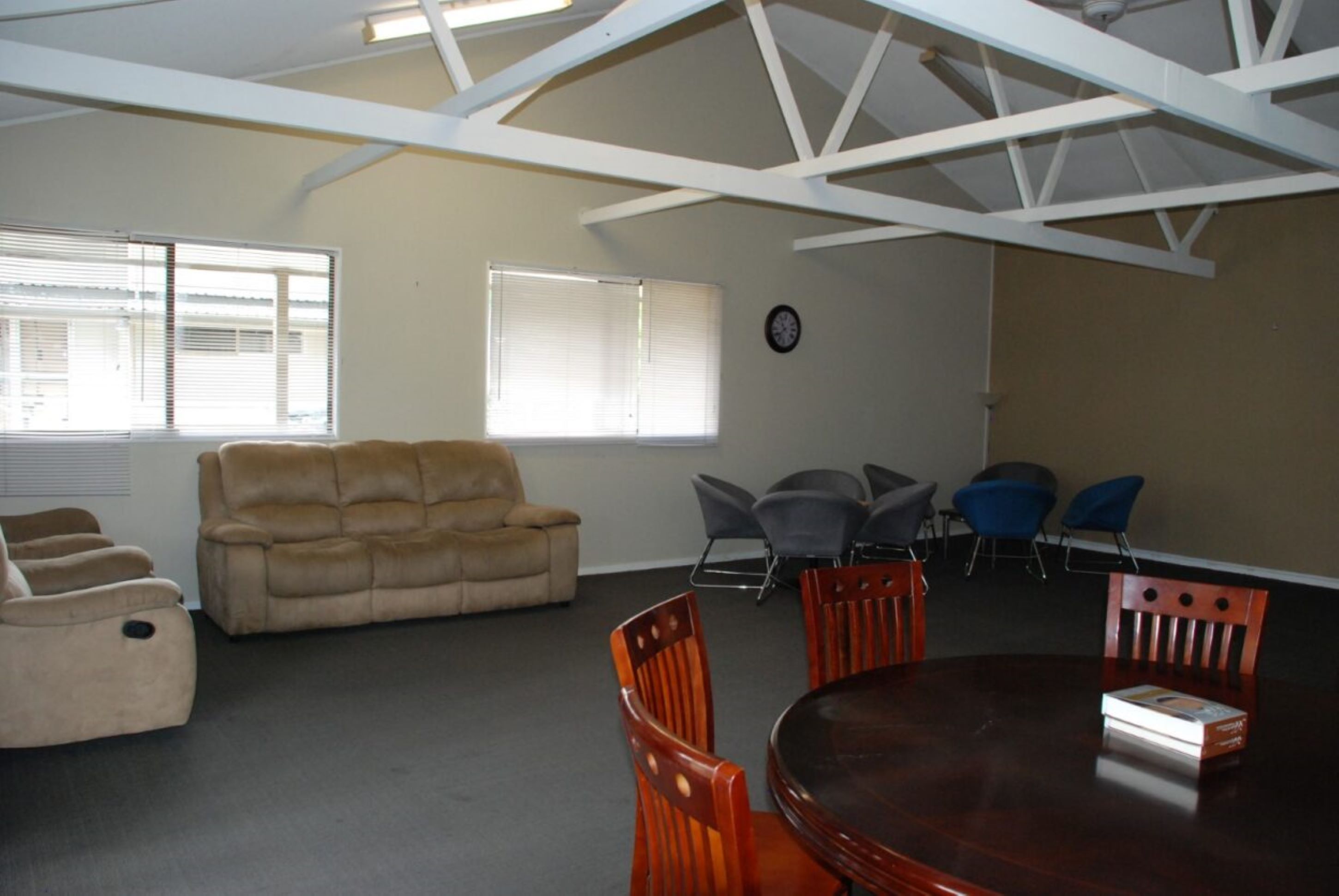 A conference room with a wooden table, four chairs, a sofa, and two windows with blinds.