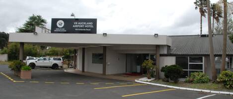 The exterior of the VR AUCKLAND AIRPORT HOTEL with a signboard, parking area, and a white pickup truck parked in front.