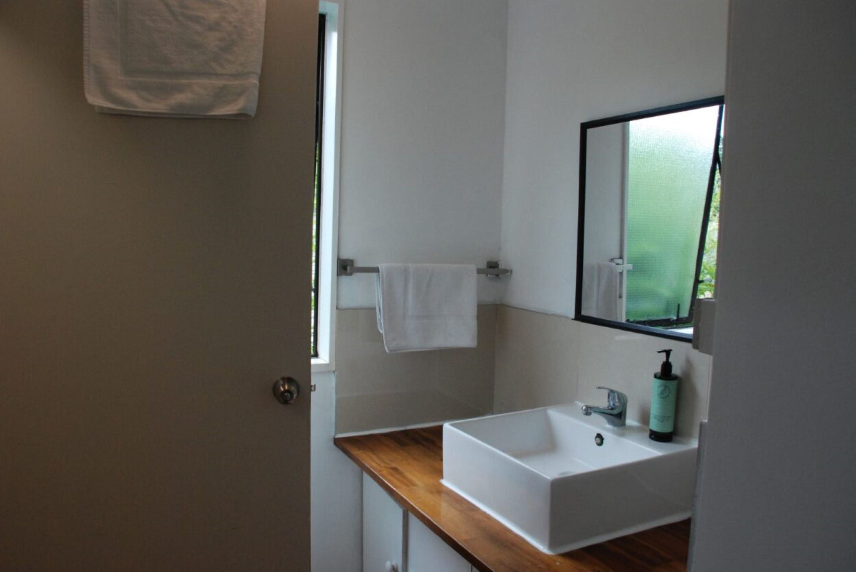 Un baño moderno con un lavamanos blanco, un espejo y una toalla colgada en un perchero.