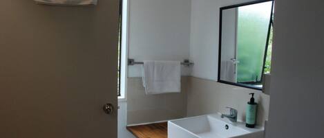 Un baño moderno con un lavamanos blanco, un espejo y una toalla colgada en un perchero.