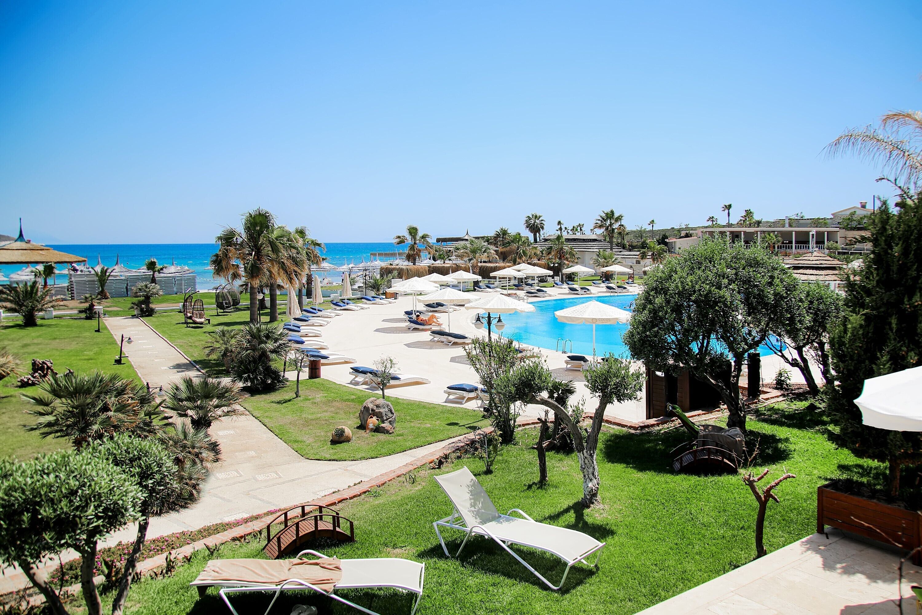 Zona de piscina en un resort con sillones de descanso, sombrillas y vista al océano.