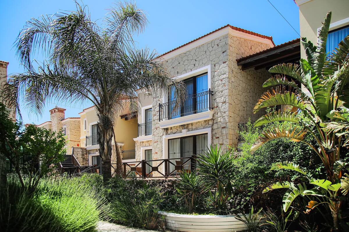 Un immeuble résidentiel à la façade en pierre, doté de balcons et d’une végétation tropicale luxuriante.