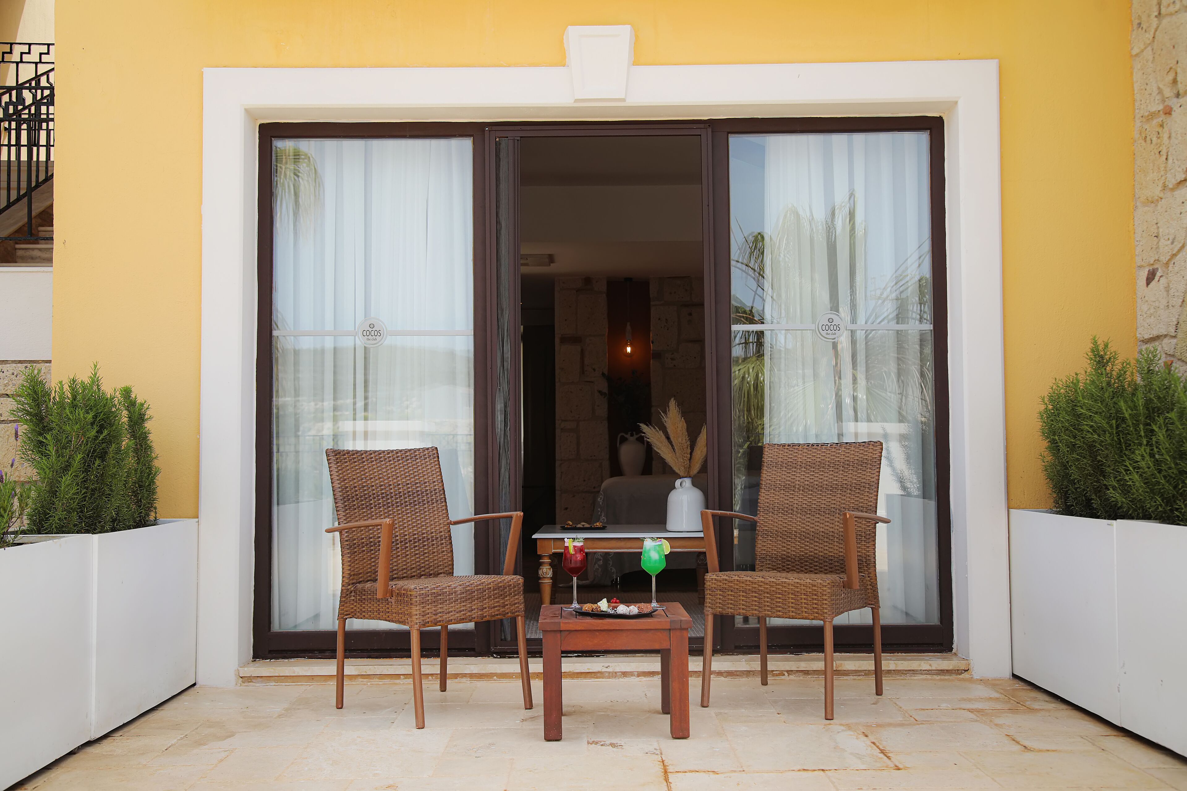 Een balkon met rieten stoelen, een tafel en een bloempot.