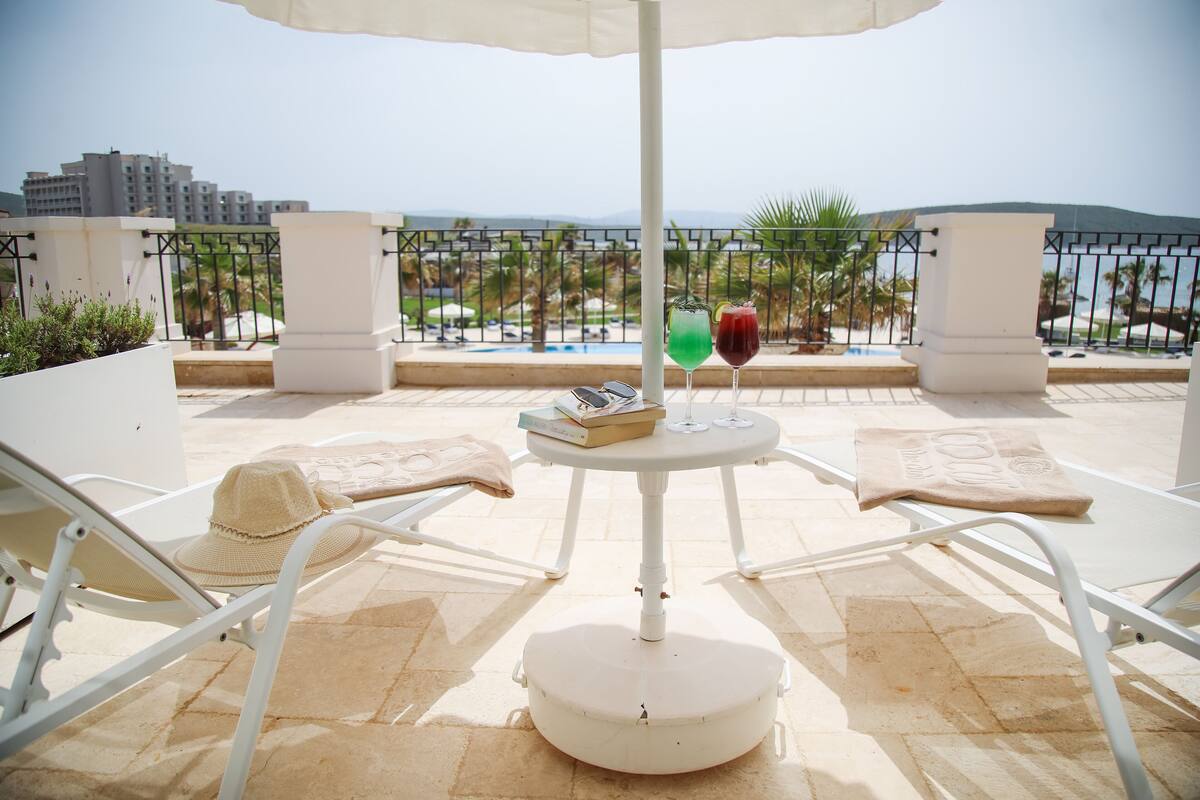Une terrasse avec une table, deux chaises, un chapeau et deux boissons.