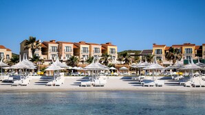 Um hotel à beira-mar com vários edifícios, guarda-sóis e espreguiçadeiras.