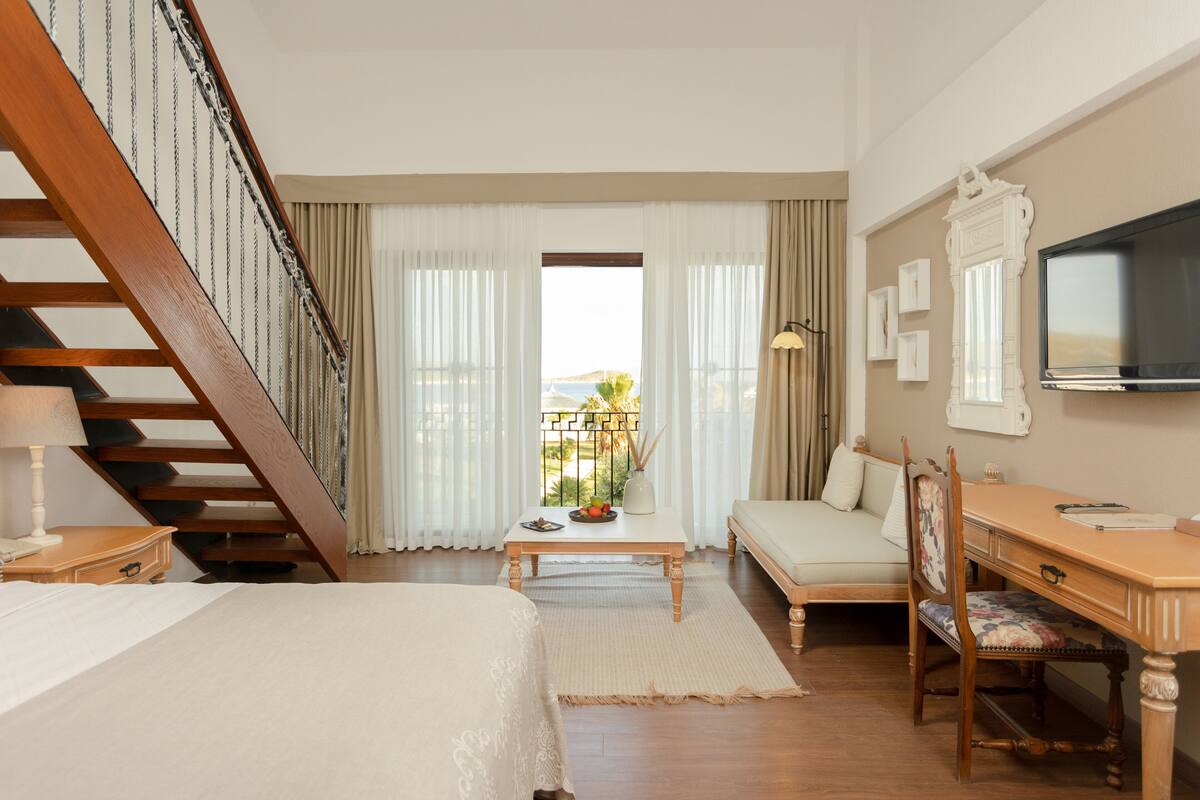 Une chambre d’hôtel avec un escalier en bois, un lit, un bureau, une chaise, un canapé et un balcon avec vue.