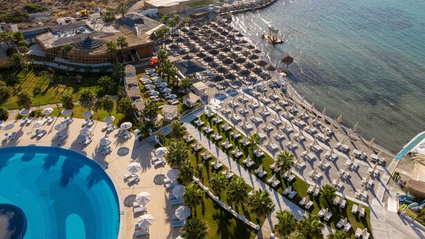 Vista aérea de um resort com uma piscina grande, várias áreas de estar na praia e uma orla.