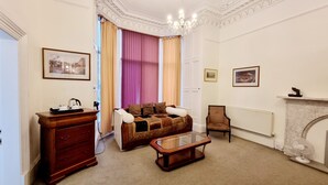 A room with a sofa, a wooden side table, a glass-top coffee table, a fireplace, and a radiator. - The Guards Hotel (Edinburgh)